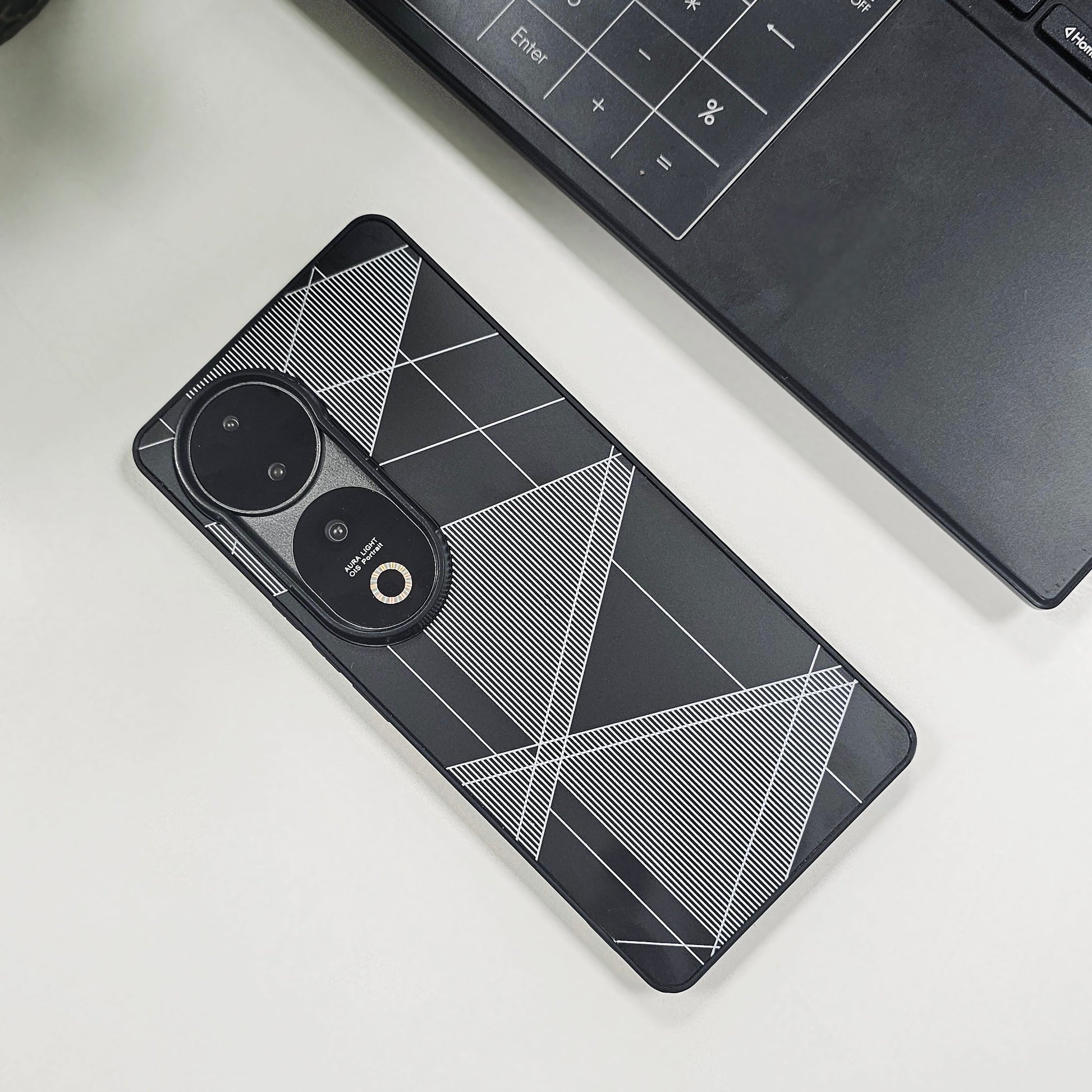 Phone case with geometric design on a white surface next to a laptop