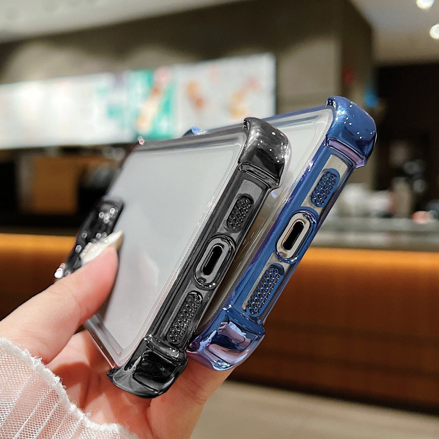 Person holding two phone cases, one clear and one blue, with a blurred indoor background.
