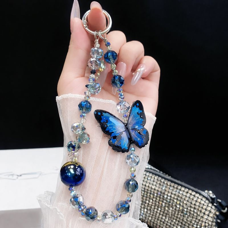 Vivo V60 5G Hand holding a decorative keychain with blue butterfly and beads against a black background