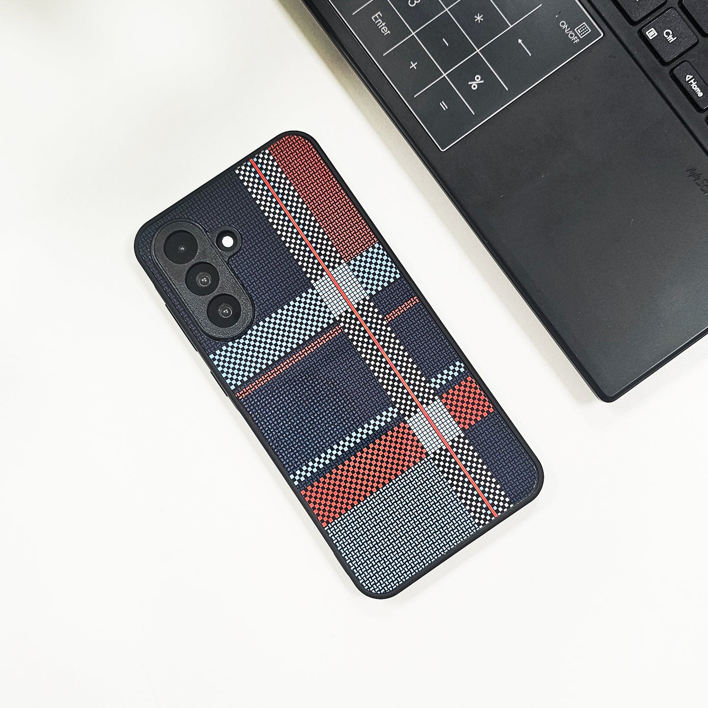Phone case with plaid pattern on a white surface next to a laptop