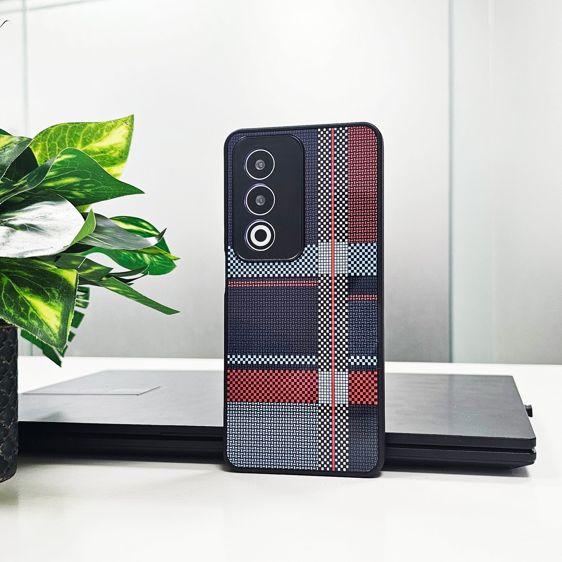 Phone case with plaid pattern on a white surface with a plant in the background
